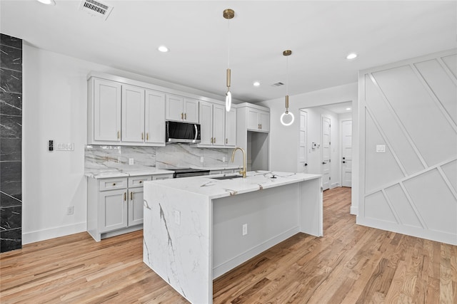 kitchen with decorative light fixtures, light wood-type flooring, stainless steel appliances, and a kitchen island with sink