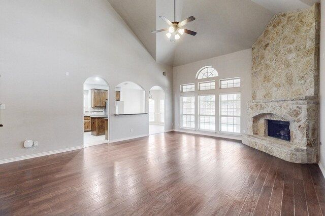 unfurnished living room featuring hardwood / wood-style floors, high vaulted ceiling, a stone fireplace, and ceiling fan