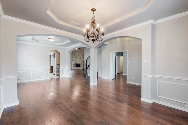 empty room with ornamental molding, a tray ceiling, a chandelier, dark hardwood / wood-style floors, and a stone fireplace