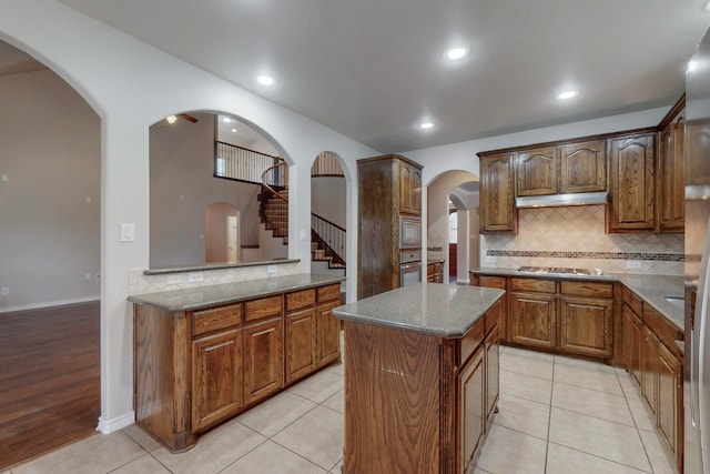 kitchen with decorative backsplash, light wood-type flooring, stainless steel appliances, stone counters, and a center island