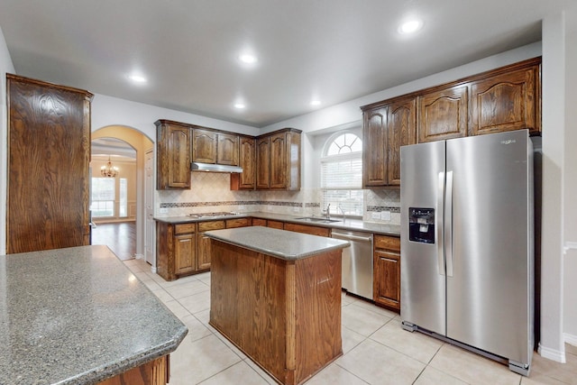 kitchen with an inviting chandelier, decorative backsplash, light tile patterned floors, appliances with stainless steel finishes, and a kitchen island