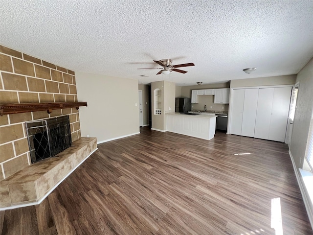 unfurnished living room featuring dark hardwood / wood-style flooring, a textured ceiling, ceiling fan, sink, and a fireplace