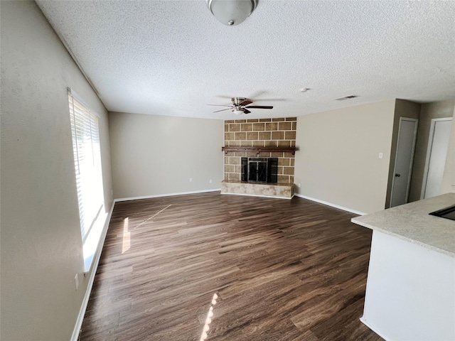 unfurnished living room with a fireplace, a textured ceiling, ceiling fan, and dark wood-type flooring