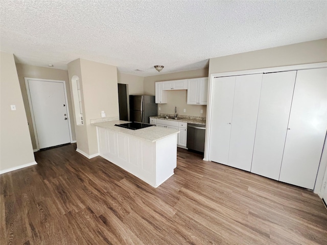 kitchen with kitchen peninsula, appliances with stainless steel finishes, a textured ceiling, white cabinets, and hardwood / wood-style flooring