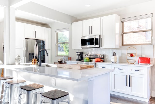 kitchen featuring appliances with stainless steel finishes, backsplash, white cabinets, and a kitchen bar