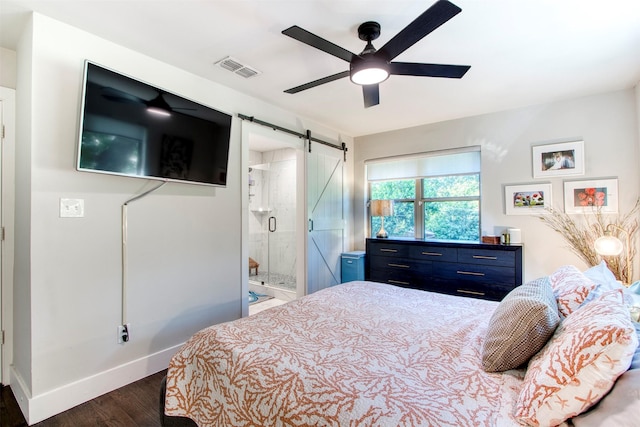 bedroom featuring a barn door, dark hardwood / wood-style floors, ceiling fan, and ensuite bath