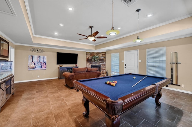 playroom with ceiling fan, pool table, a raised ceiling, a stone fireplace, and ornamental molding