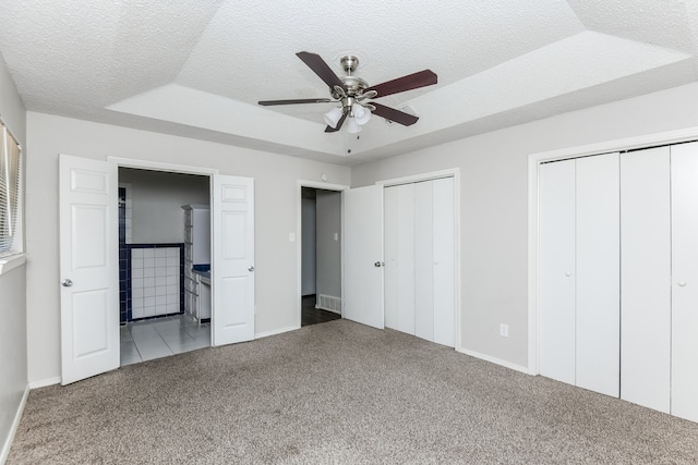 unfurnished bedroom with a raised ceiling, multiple closets, ceiling fan, and carpet