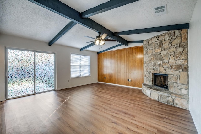 unfurnished living room with ceiling fan, a fireplace, lofted ceiling with beams, light hardwood / wood-style floors, and a textured ceiling