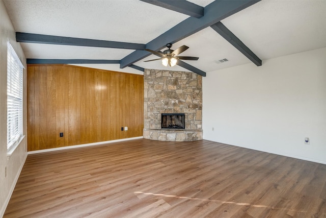 unfurnished living room featuring hardwood / wood-style flooring, ceiling fan, vaulted ceiling with beams, a textured ceiling, and a stone fireplace