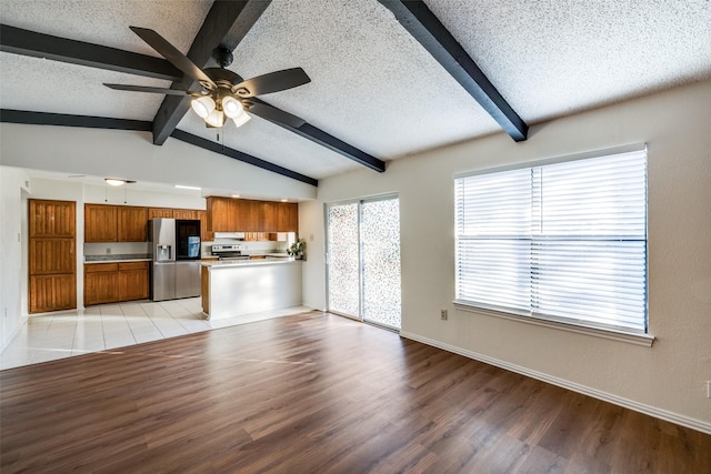 unfurnished living room with vaulted ceiling with beams, ceiling fan, a textured ceiling, and light wood-type flooring