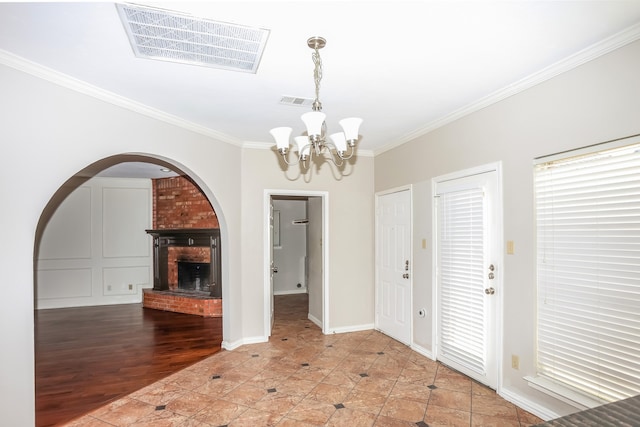 entryway featuring hardwood / wood-style floors, a brick fireplace, crown molding, and a notable chandelier