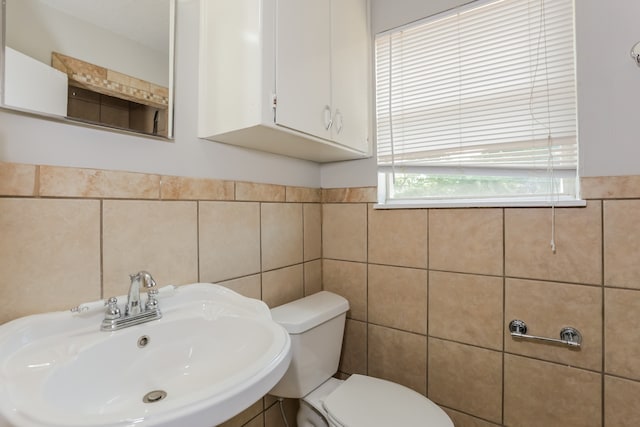 bathroom with toilet, sink, and tile walls