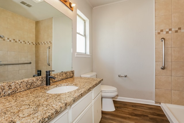 bathroom with vanity, toilet, ornamental molding, tiled shower, and wood-type flooring