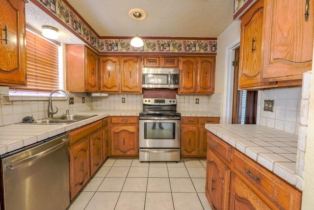 kitchen with appliances with stainless steel finishes, a textured ceiling, tile countertops, and sink