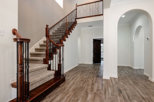 foyer featuring wood-type flooring, a towering ceiling, a wealth of natural light, and ornamental molding