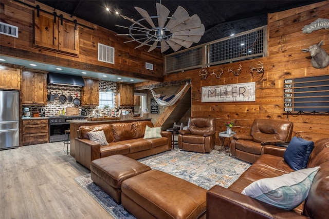 living room featuring a high ceiling, wood walls, ceiling fan, and light hardwood / wood-style flooring