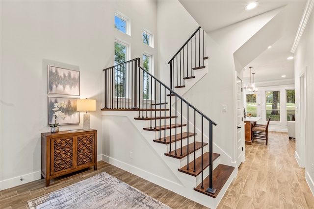 stairway with hardwood / wood-style floors, a towering ceiling, an inviting chandelier, and crown molding