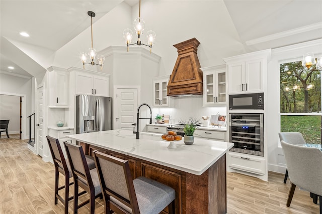 kitchen featuring custom exhaust hood, a kitchen island with sink, white cabinets, light hardwood / wood-style floors, and stainless steel appliances