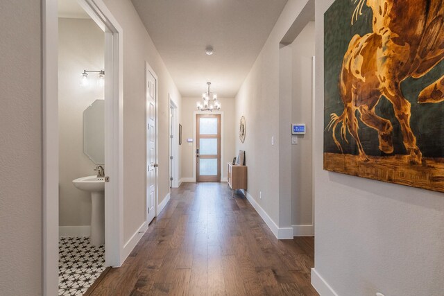 corridor with a notable chandelier, sink, and dark wood-type flooring