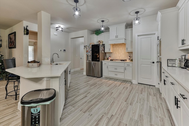 kitchen featuring appliances with stainless steel finishes, a kitchen island with sink, sink, white cabinetry, and hanging light fixtures