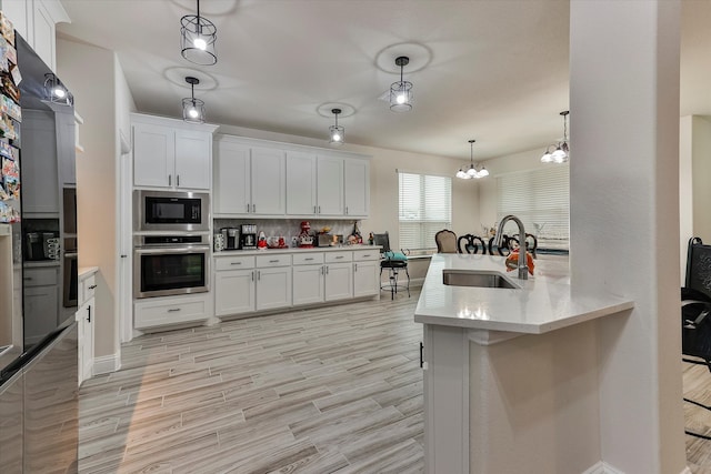 kitchen with appliances with stainless steel finishes, sink, light hardwood / wood-style flooring, white cabinets, and hanging light fixtures