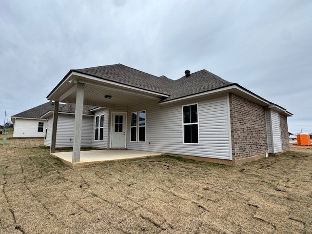 back of house with a yard, a patio area, brick siding, and a shingled roof