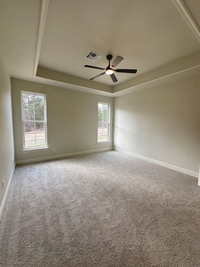 carpeted empty room featuring a ceiling fan, visible vents, a tray ceiling, and baseboards