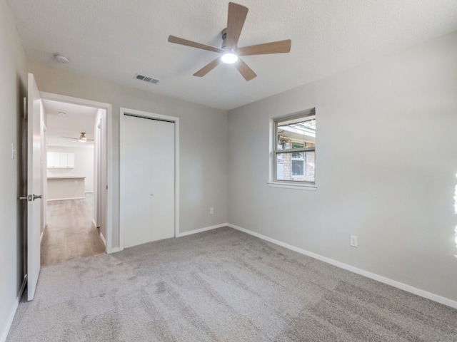 unfurnished bedroom with light carpet, a textured ceiling, a closet, and ceiling fan