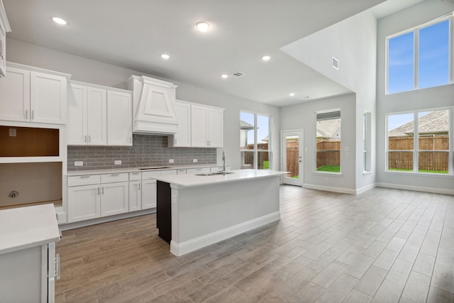 kitchen with white cabinetry, sink, a kitchen island with sink, custom range hood, and light wood-type flooring