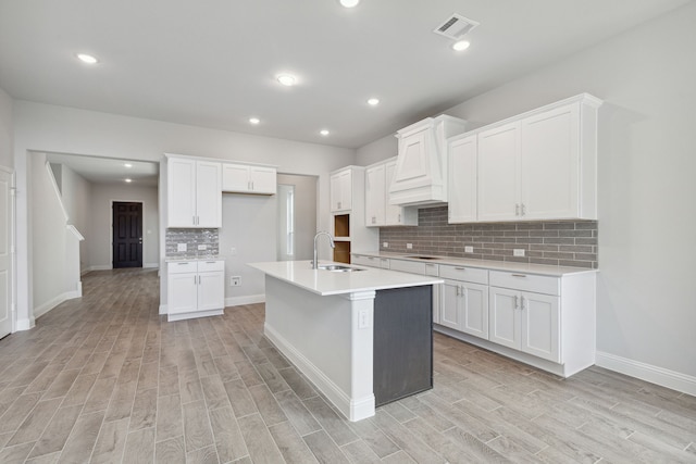 kitchen featuring white cabinets, sink, an island with sink, and light hardwood / wood-style flooring