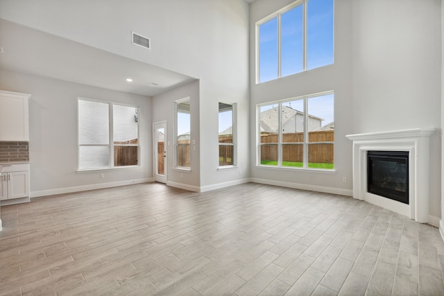 unfurnished living room featuring a towering ceiling and light hardwood / wood-style flooring