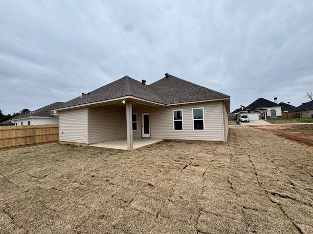 back of property featuring roof with shingles, a patio, a lawn, and fence