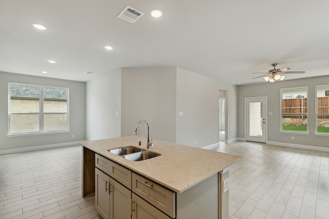 kitchen featuring a healthy amount of sunlight, light stone countertops, sink, and a kitchen island with sink