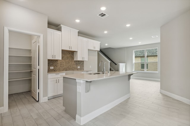 kitchen with a kitchen bar, sink, white cabinetry, a kitchen island with sink, and backsplash