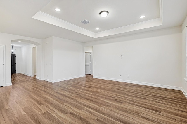 empty room with hardwood / wood-style flooring, a tray ceiling, and crown molding