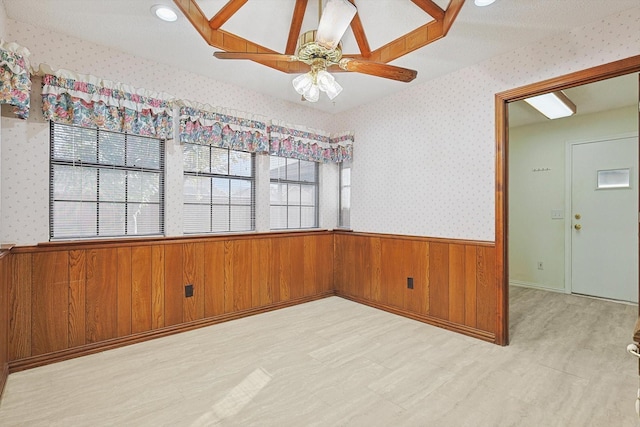 unfurnished room featuring light hardwood / wood-style flooring, wooden walls, and ceiling fan