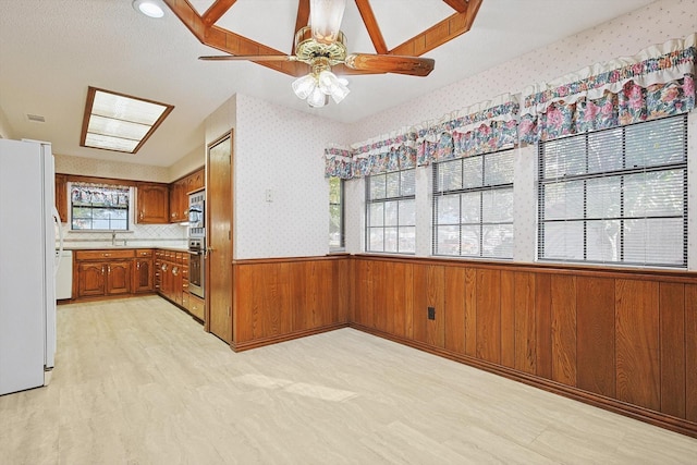 kitchen featuring wooden walls, sink, ceiling fan, stainless steel appliances, and light hardwood / wood-style flooring