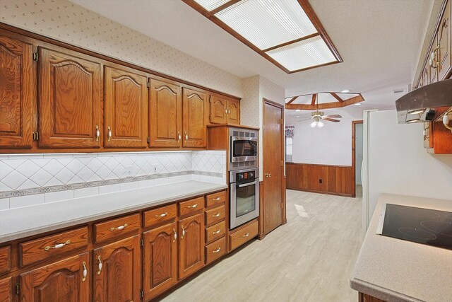 kitchen featuring wood walls, appliances with stainless steel finishes, ceiling fan, light hardwood / wood-style floors, and decorative backsplash