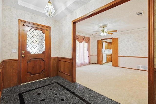 entrance foyer with ceiling fan, a tray ceiling, a textured ceiling, and carpet flooring