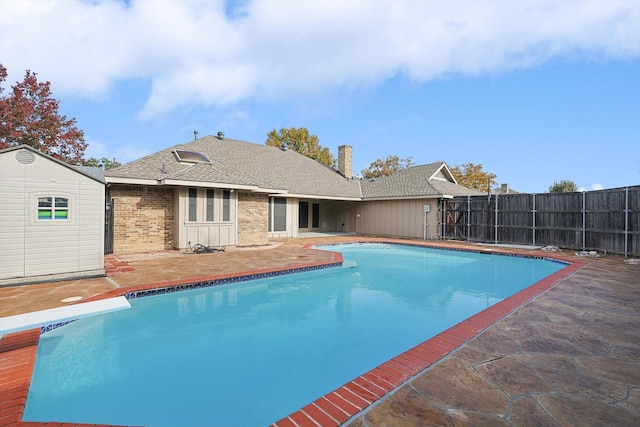 view of swimming pool with a shed, a diving board, and a patio