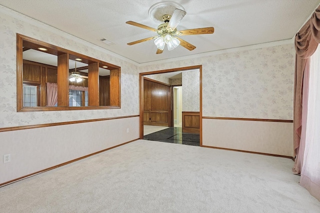 carpeted empty room with ceiling fan, crown molding, and a textured ceiling