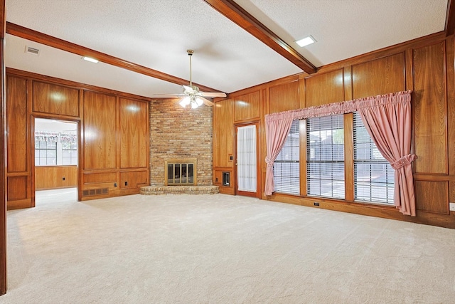 unfurnished living room featuring a fireplace, wood walls, beamed ceiling, light colored carpet, and a textured ceiling