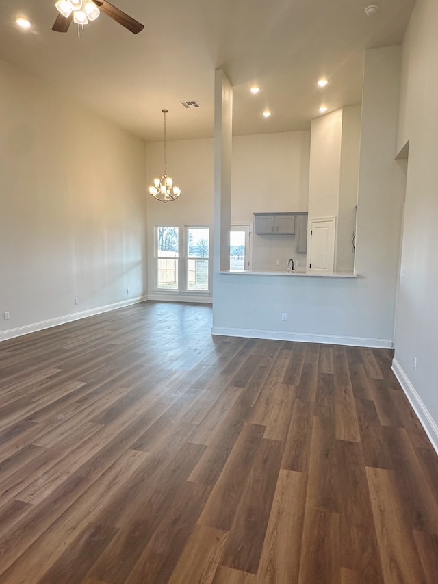 unfurnished living room featuring ceiling fan with notable chandelier, dark wood-type flooring, and a high ceiling