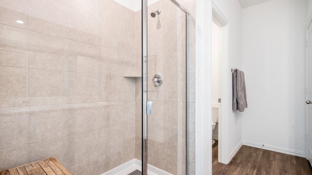 bathroom featuring wood-type flooring, toilet, and a shower with door