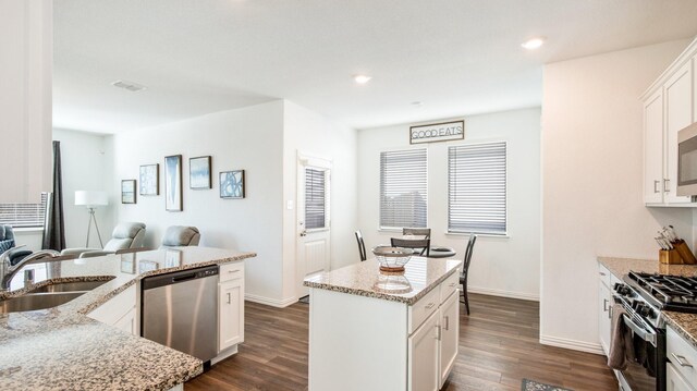 kitchen with sink, dark wood-type flooring, stainless steel appliances, light stone counters, and a kitchen island