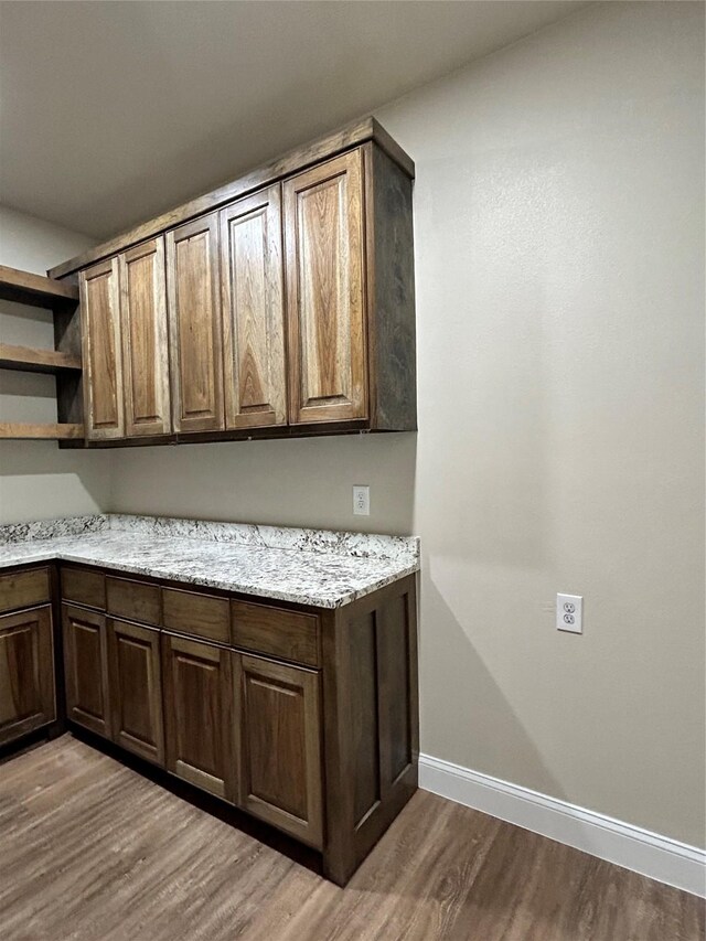 interior space with dark brown cabinetry, light stone counters, and light hardwood / wood-style flooring