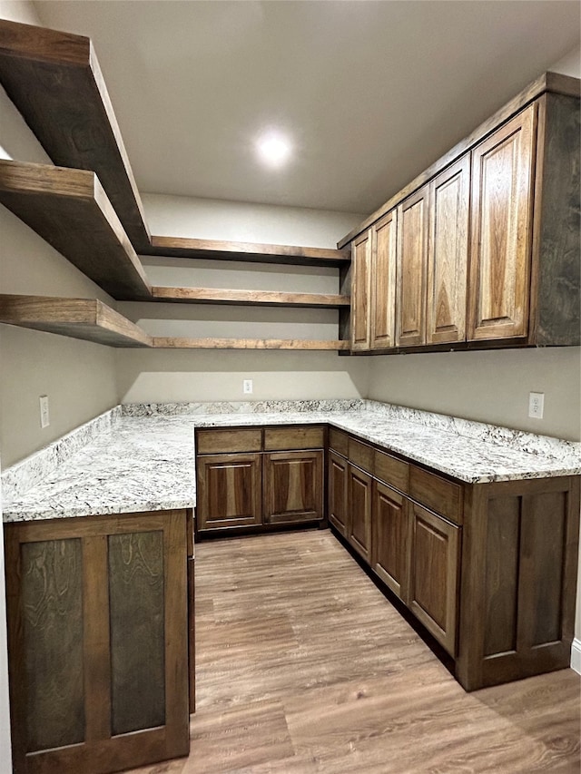 bar with dark brown cabinets, light stone counters, and light hardwood / wood-style flooring