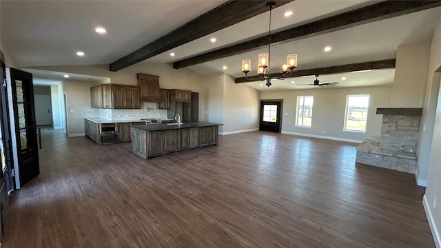 kitchen with vaulted ceiling with beams, dark hardwood / wood-style floors, decorative backsplash, a center island with sink, and ceiling fan with notable chandelier