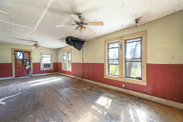 empty room with ceiling fan, plenty of natural light, wood-type flooring, and a textured ceiling